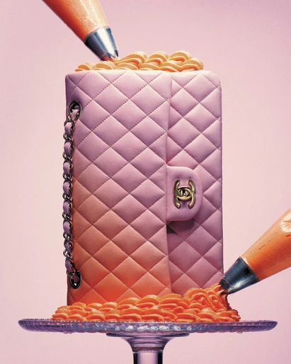 Novelty quilted handbag cake with pastel pink frosting ombre effect on a glass pedestal stand being decorated with orange frosting.