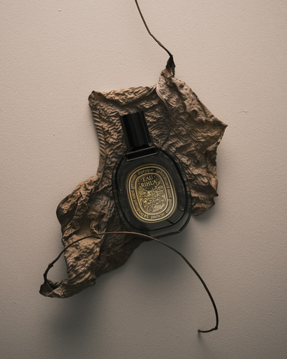 Elegant studio shot of a perfume bottle on a textured leaf against a neutral background, highlighting beauty and product design.