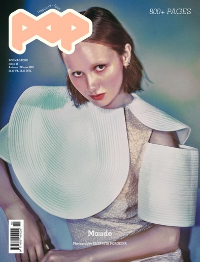 Magazine cover featuring a model with short brown hair, wearing a dress with a large white collar, posing against a blue background.