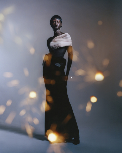 Portrait of a Black fashion model in couture dress posing in a photo studio with bokeh lights and cool-toned background lighting.