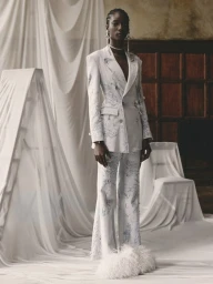 Model in white patterned suit with feather shoes standing in draped interior by Olivia Giles