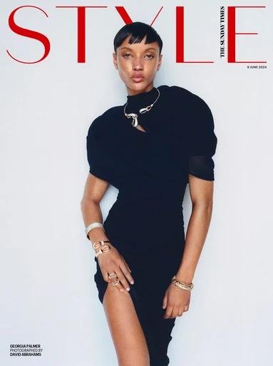 Model in a black dress wearing metallic bracelets and a sculptural necklace against a white background
