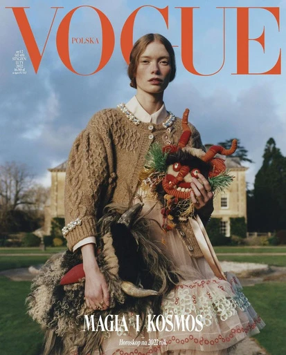 Vogue Polska cover featuring a woman in a cardigan and dress, holding a ram and a devil mask, set against a stately home and cloudy sky.