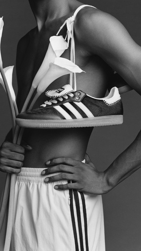 Monochrome image of a Black male torso with Adidas sneaker and white calla lilies, hands on waist, wearing shorts, and studio setting.