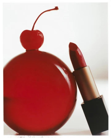 Close-up product photography of red lipstick next to a spherical glass ornament topped with a cherry