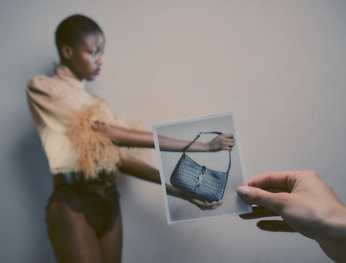Editorial fashion shot of a Black woman posing with a handbag photo in a studio, showcasing modern style and muted tones.