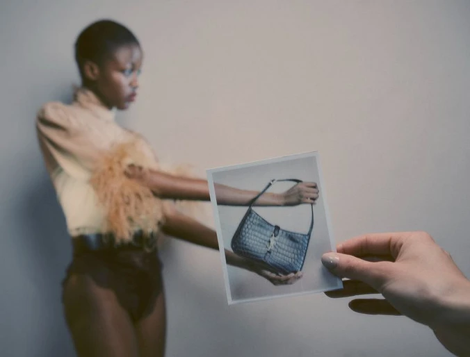 Editorial fashion shot of a Black woman posing with a handbag photo in a studio, showcasing modern style and muted tones.