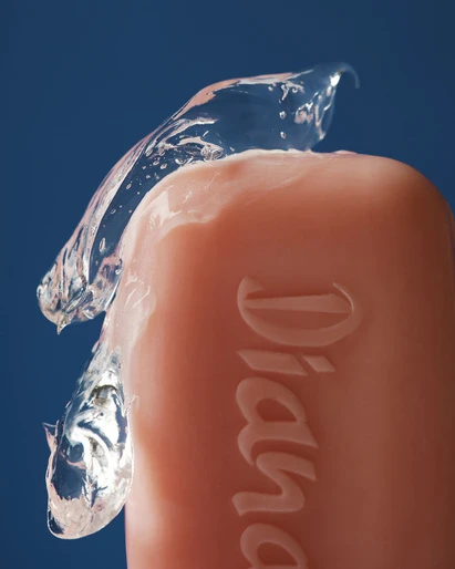 Soap bar with clear liquid on top against a dark blue background, macro shot. Beauty and hygiene product with textured surface.