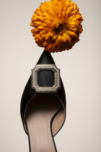 Pointed-toe black pump with jewel buckle and an orange flower, studio shot. Sophisticated women's footwear for special occasions.