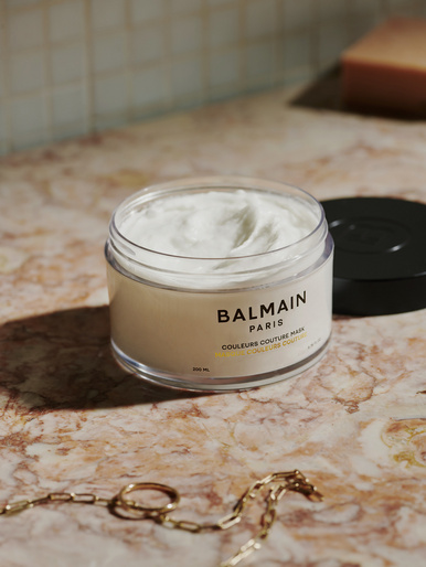 Balmain Paris hair mask product shot on a marble surface with a gold chain necklace and warm, diffused lighting.