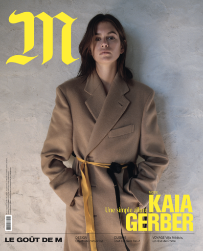 Magazine cover featuring Kaia Gerber in a tan trench coat with a yellow and black belt, against a textured grey backdrop.