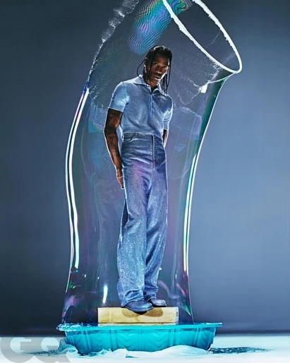 Adult male model in shimmering blue outfit stands in a bubble in a photo studio for a magazine cover, GQ logo in corner.