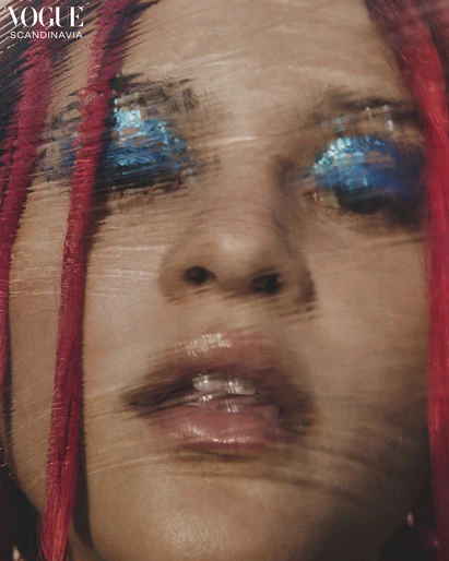 Fashion editorial close-up of a woman with bright blue glitter eyeshadow and vibrant red hair, shot for Vogue Scandinavia.
