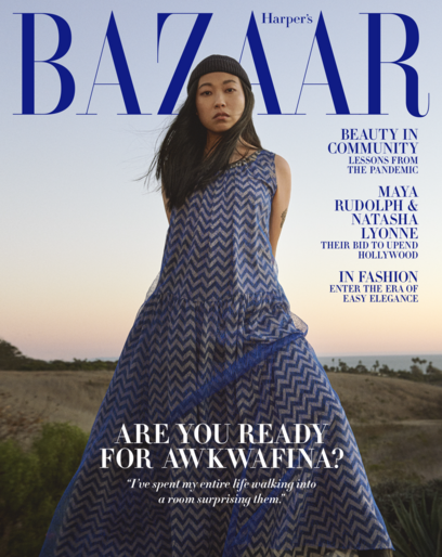 Awkwafina poses in a full-length blue-patterned dress for a Harper's Bazaar cover, set against a natural landscape with a twilight sky.