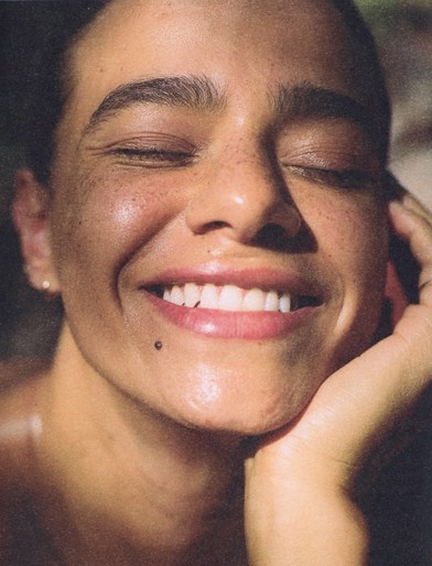 Close-up portrait of a smiling woman with eyes closed and hand resting against her cheek by Jc Molina