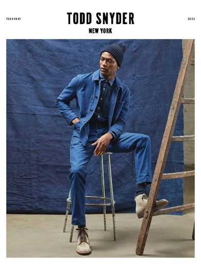 Man in blue denim outfit sits on stool next to ladder against blue backdrop. Fashion shot for Todd Snyder New York 2021.