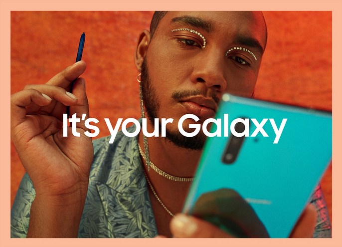 A person holds a teal smartphone and dark-blue stylus, set against an orange background with 'It's your Galaxy' text overlay.