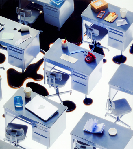 Overhead shot of numerous metal office desks and chairs on a bright white surface with abstract black markings and office supplies.