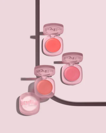 Four Kylie Cosmetics blushes in pink packaging are arranged on a light pink surface with linear shadows creating a geometric composition.