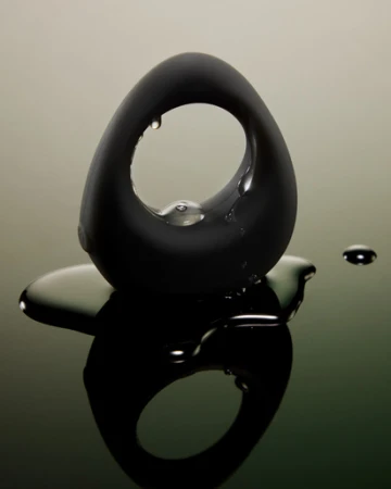 Sleek, black, ovoid object with a central hole, adorned with water droplets, reflecting on a glossy surface with a blurred background.