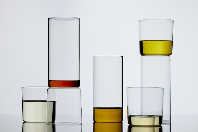 Still life of clear glasses with colorful liquids stacked in a minimalistic composition against a bright, neutral backdrop, studio shot.