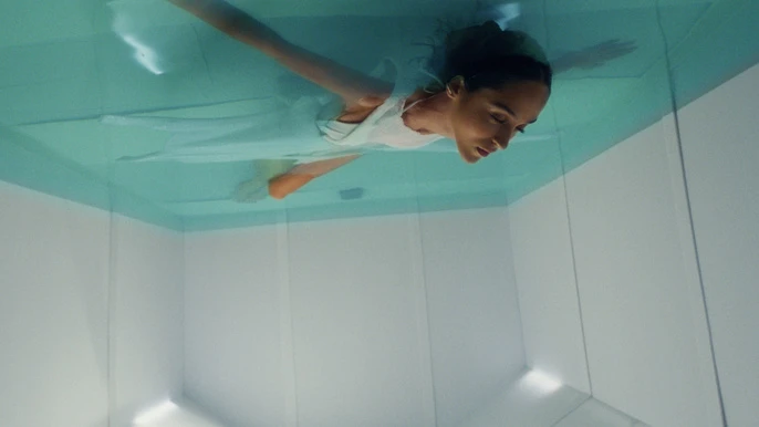 Woman in a white dress floats serenely underwater in a modern, minimalist pool illuminated by soft, diffused light.