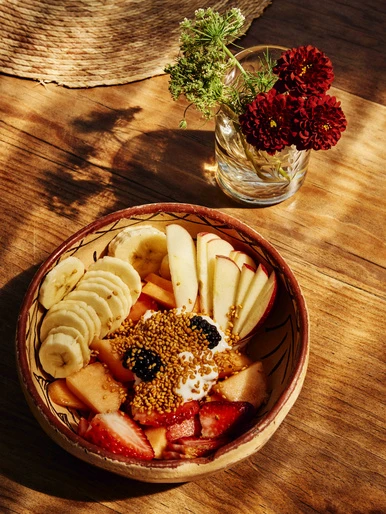 A bowl of fresh fruit with yogurt and flowers on a wooden table bathed in natural light, showcasing a healthy and vibrant food scene.