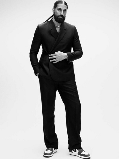 Man in a black double-breasted suit and sneakers standing against a plain white background, styled by Julia Brenard.