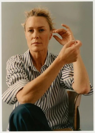 Woman wearing a blue and white striped shirt sitting on a chair against a plain grey studio backdrop