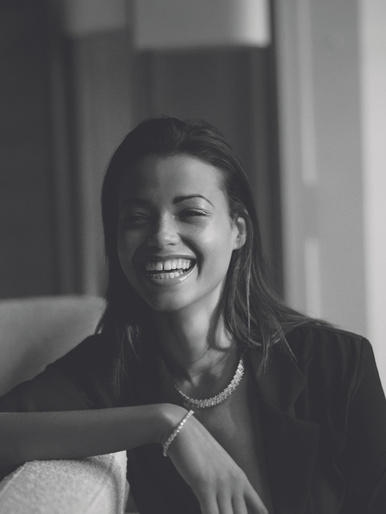 Black and white portrait of a smiling woman wearing a necklace and bracelet styled by Julia Brenard.