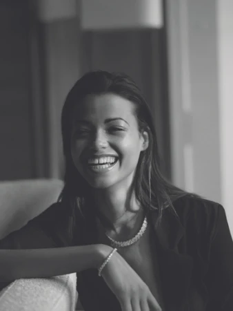 Black and white portrait of a smiling woman wearing a necklace and bracelet styled by Julia Brenard.