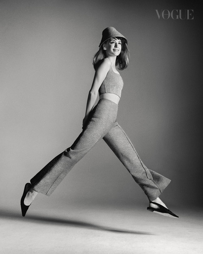 Monochrome fashion portrait of a smiling woman mid-air jumping, wearing a matching knit crop top, trousers, and hat.