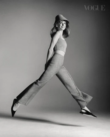 Monochrome fashion portrait of a smiling woman mid-air jumping, wearing a matching knit crop top, trousers, and hat.
