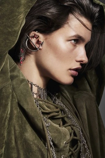Close-up of a woman in an olive green hooded velvet top and silver and red beaded jewelry, side profile view with soft lighting.