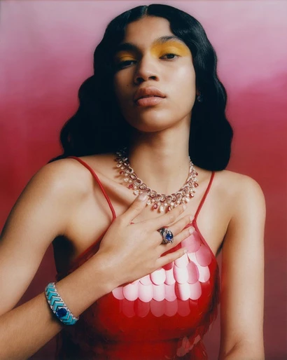 Elegant model wearing a red sequined dress and jewelry poses against a pink backdrop in a beauty and fashion style portrait.