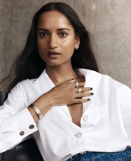 Portrait of an East Indian woman with long dark hair wearing a white button-down shirt, jewelry, and dark nail polish.