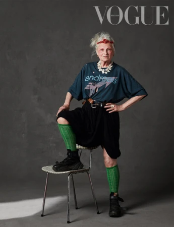Fashion editorial shot of older woman, Vivienne Westwood, wearing a graphic t-shirt, black skirt, knee socks, and sneakers, sitting on a chair.