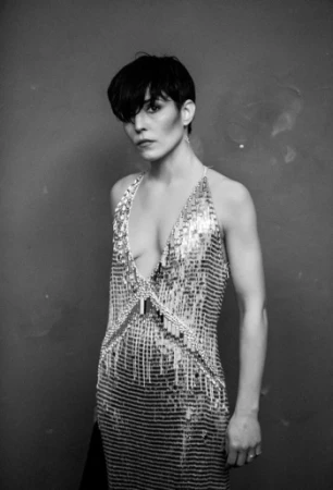 Monochrome portrait of a woman with dark short hair wearing a shimmering sequined halter dress against a textured dark background.
