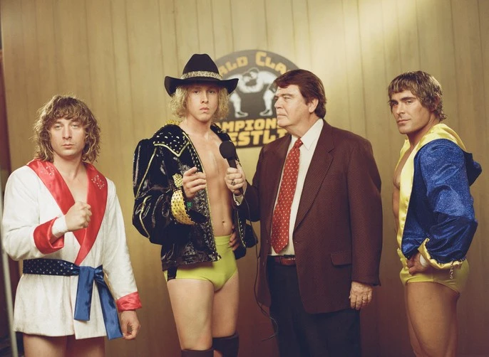 Wrestlers and announcer pose during interview with bright lighting in front of World Class Championship Wrestling logo at event.