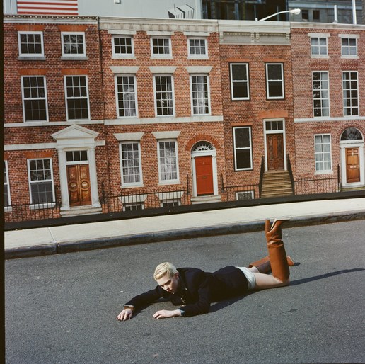 Model with blonde hair lying on an asphalt street wearing tall brown leather boots and a dark jacket styled by Cece Liu in London.