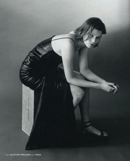 Monochrome portrait of a woman in a long black dress sitting on a wooden cube in a studio, exuding a classic and elegant aesthetic.
