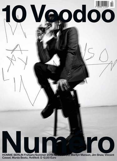 Black and white magazine cover featuring an adult posing on a stool with bold fonts and stylistic text overlays against a neutral backdrop.