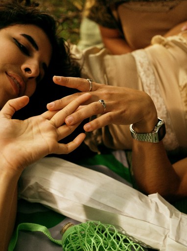 Close-up of a person lying down with rings on fingers and a metal wristwatch, styled by Cece Liu in London.