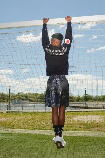 Athletic Black man hangs from a soccer net in athletic wear with the words "It takes a little more to be a champion"
