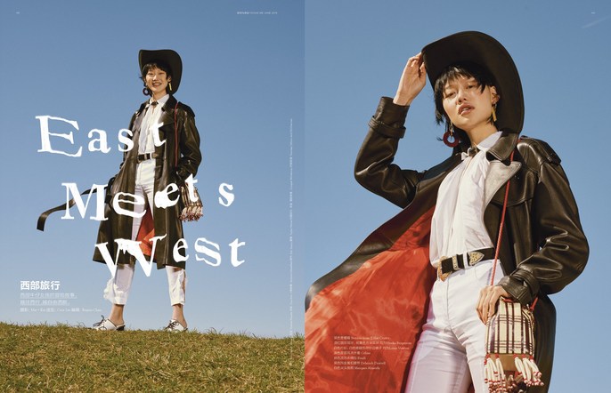 Fashion editorial shot of a woman in a cowboy hat, leather coat, and white pants standing on a grassy hill against a blue sky.