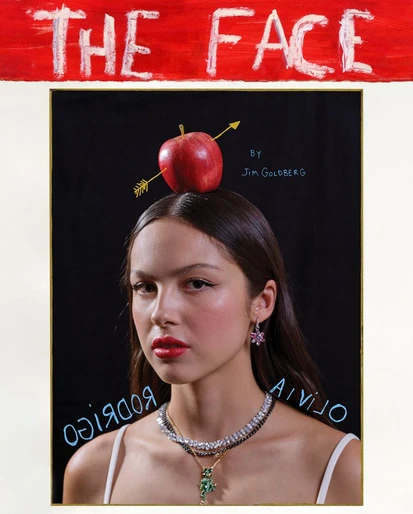 A portrait of Olivia Rodrigo with an apple pierced by an arrow on her head, posing in front of a black background.