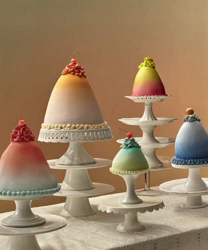 Display of ombre-frosted cakes, each adorned with a cherry and presented on individual white cake stands of varying heights.