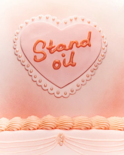 Pink cake with heart-shaped frosting and cursive text reading 'Stand Oil', featuring pearl-like decorations on a smooth, light pink background.