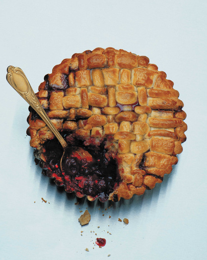 Overhead shot of blueberry pie with golden crust, filling partially scooped out with a vintage gold spoon against light blue backdrop.