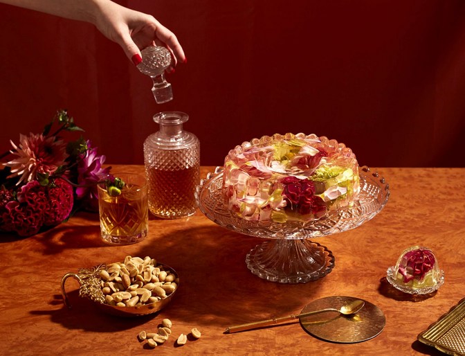 Crystal servingware and edible flower gelatin dessert with a human hand holding a crystal decanter topper in a staged food photography setting.